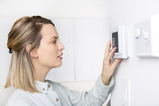 A woman adjusting a thermostat.