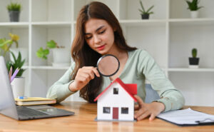 A woman using a magnifying glass to inspect a small model of a house.